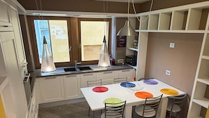 A modern kitchen with white cabinets, a dining table with colorful placemats, and pendant lights. - At the foot of the Mortirolo (Mazzo di Valtellina)