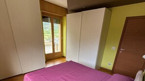 A bedroom with a large bed, wooden flooring, a sliding door to a balcony, and a wardrobe. - At the foot of the Mortirolo (Mazzo di Valtellina)