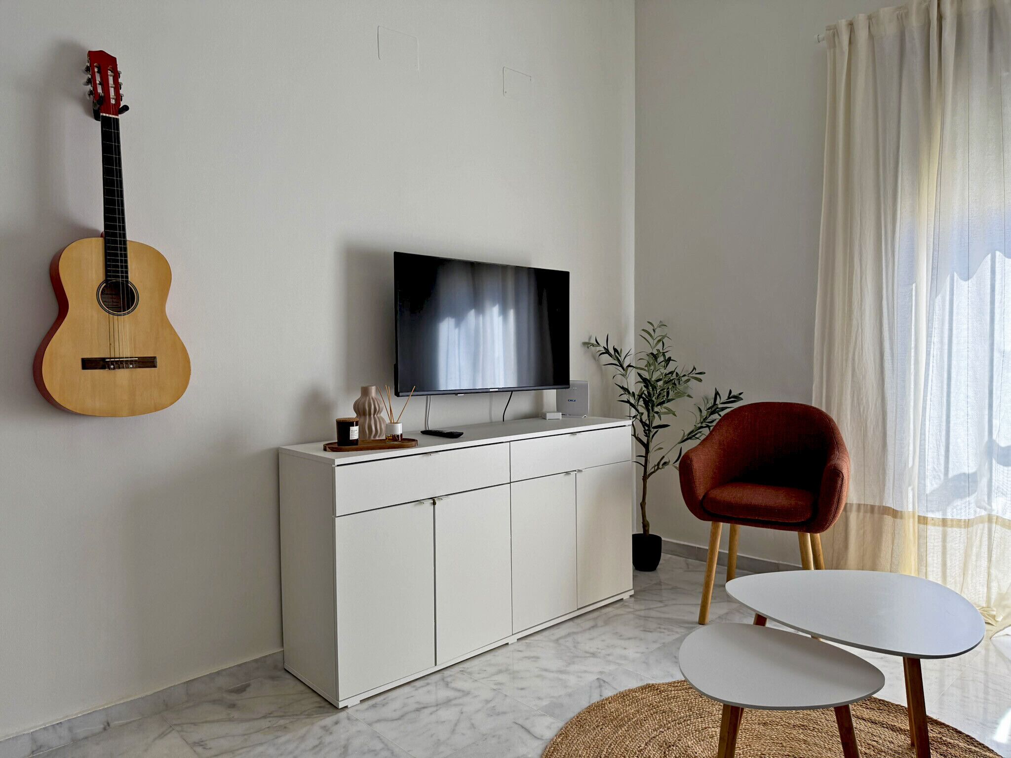 Een woonkamer met een gitaar, televisie, rode stoel en een klein tafeltje.