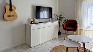 Ein Wohnzimmer mit Gitarre, Fernseher, rotem Sessel und einem kleinen Tisch.