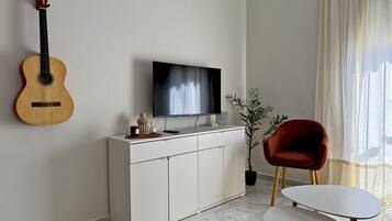 Een woonkamer met een gitaar, televisie, rode stoel en een klein tafeltje.
