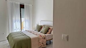 Ein Schlafzimmer mit Bett, Fenster mit Vorhängen, Nachttisch und Lichtschalter.