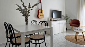 Ein Essbereich mit einem weißen Tisch, schwarzen Stühlen, einer Gitarre und einem Fernseher auf einem Schrank.