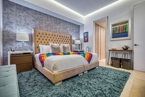 Une chambre à coucher moderne avec une tête de lit capitonnée, une couverture colorée, un tapis moelleux et une table de chevet au design minimaliste.