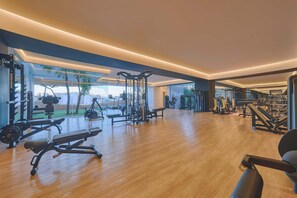 Een ruime fitnessruimte met diverse trainingsapparaten, grote ramen en een houten vloer.