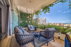 A balcony with wicker furniture, a round table, and a view of the cityscape and ocean.