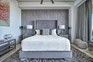A modern bedroom with a large bed, two bedside lamps, a textured headboard, and a large window with curtains.