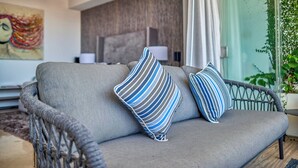 A grey sofa with blue and white striped pillows, a ceiling fan, a painting, and a potted plant. - Luxurious Condo at SOHO with Panoramic Romantic Zone Views (Puerto Vallarta)