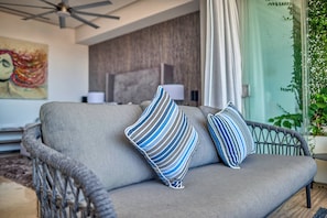 A grey sofa with blue and white striped pillows, a ceiling fan, a painting, and a potted plant.