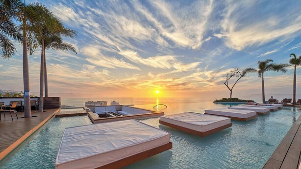 A rooftop infinity pool with sun loungers and a view of the sunset over the ocean. - Luxurious Condo at SOHO with Panoramic Romantic Zone Views (Puerto Vallarta)