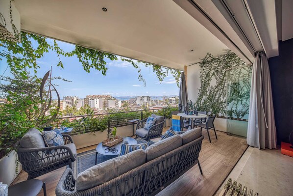 Un balcón con mobiliario de mimbre, una mesa de vidrio y vistas a la ciudad.