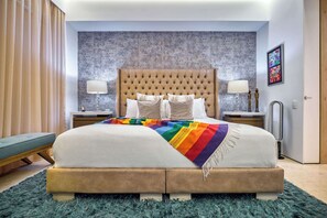 A bedroom with a tufted headboard, a bed with a rainbow-patterned blanket, two bedside tables with lamps, and a blue shaggy rug. - Luxurious Condo at SOHO with Panoramic Romantic Zone Views (Puerto Vallarta)