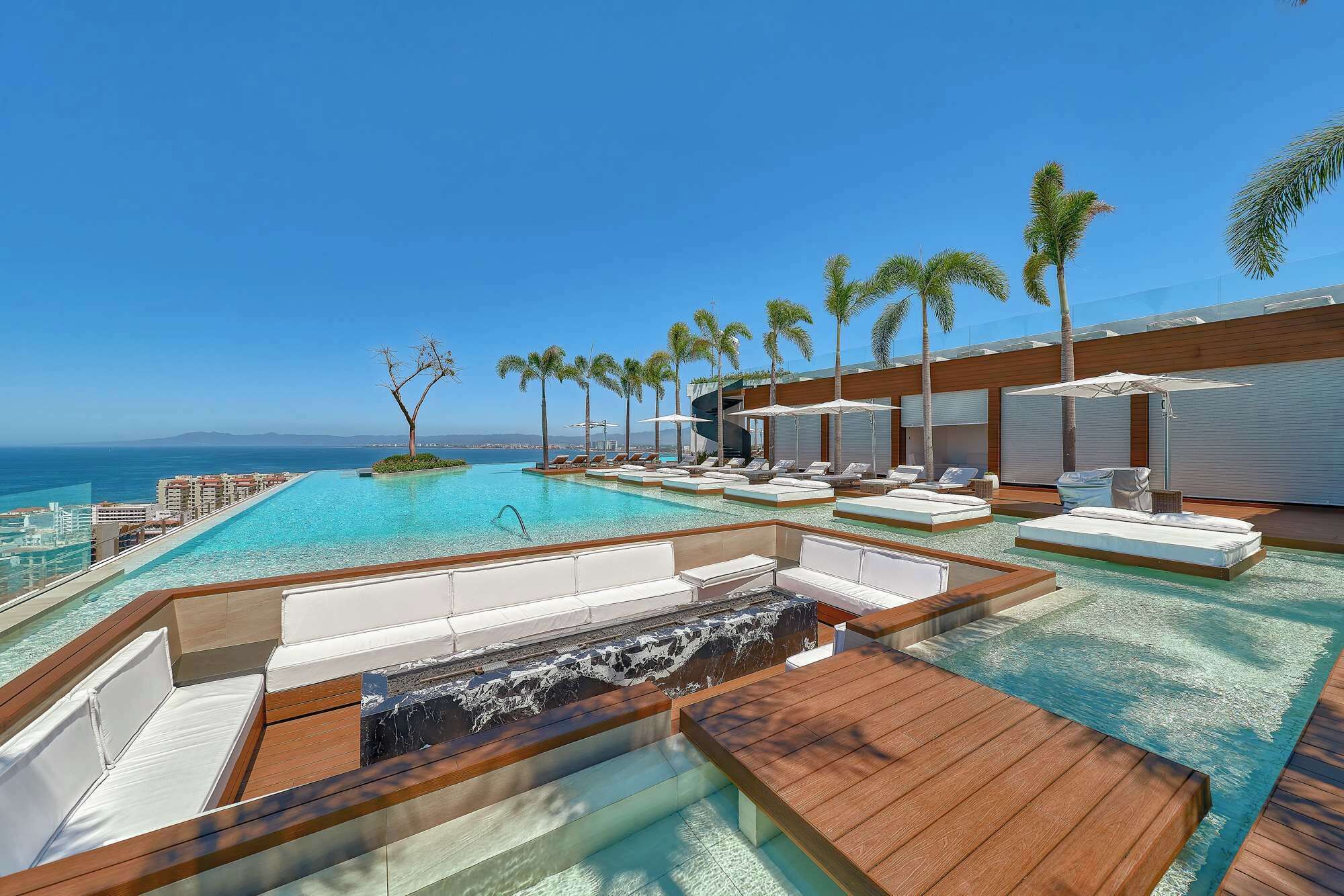 A resort pool area with clear blue water, lounge chairs, and palm trees.
