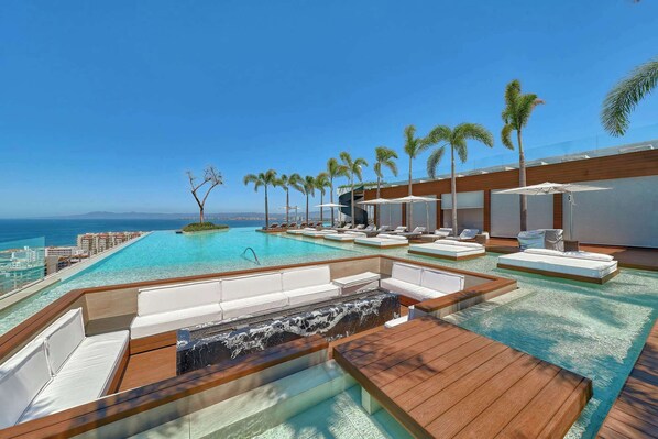 A resort pool area with clear blue water, lounge chairs, and palm trees.