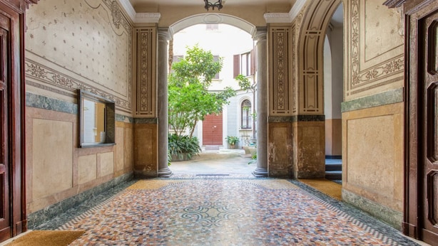 A hallway with a tiled floor, columns, and a view of an outdoor area with a tree.