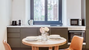 A kitchen with a dining table set for two, a window with a view of greenery, and a microwave on the countertop.