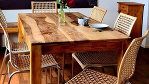 Uma área de refeições com mesa de madeira, cadeiras de vime e um quadro na parede com pedras e água.