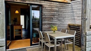 A wooden exterior wall, a sliding glass door leading to a room, and a table with chairs outside.