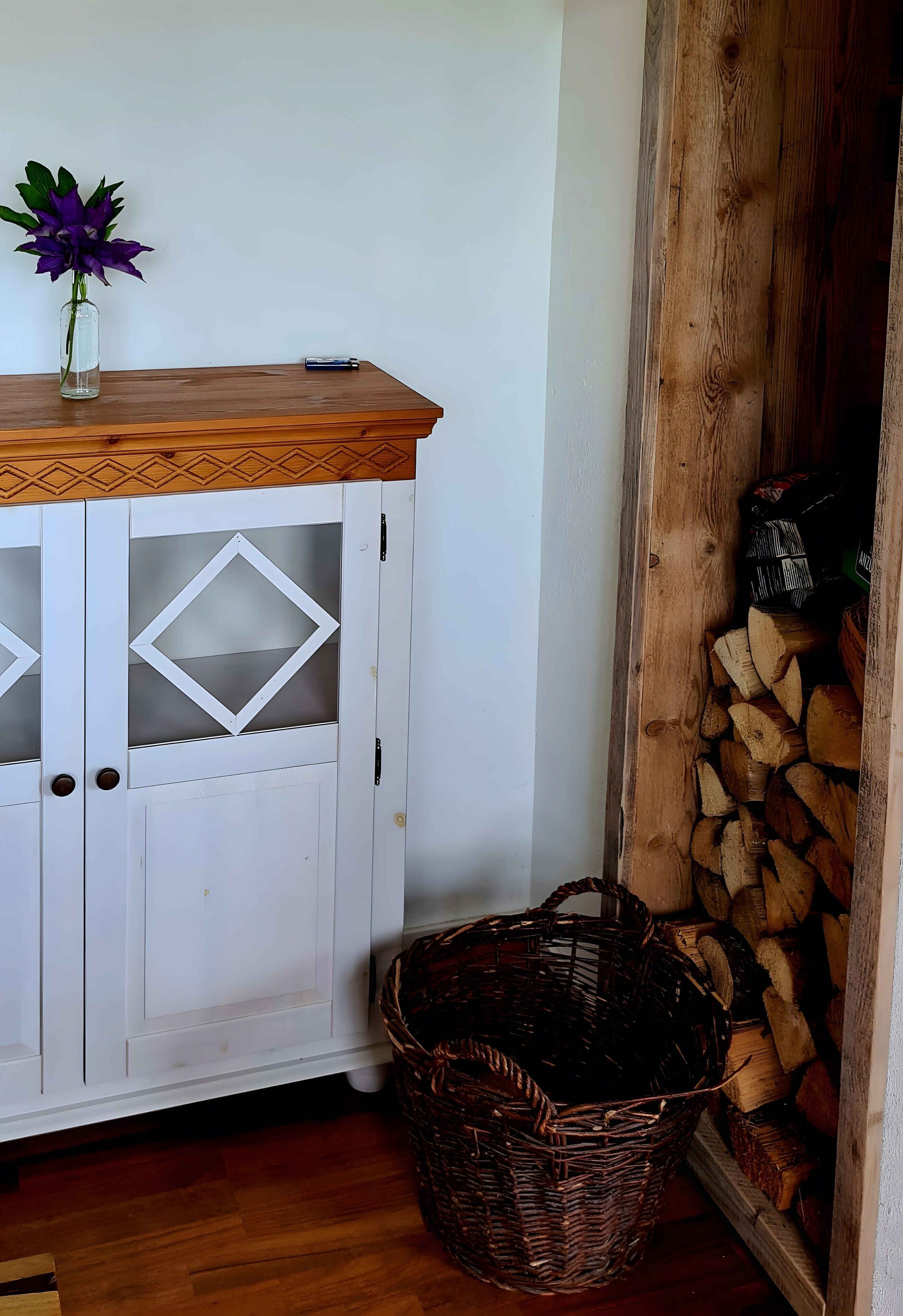 A wooden cabinet with glass doors, a wicker basket, and a vase with purple flowers.