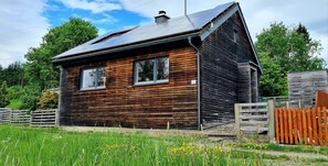 A wooden cabin with a sloped roof, large windows, and a fenced yard.