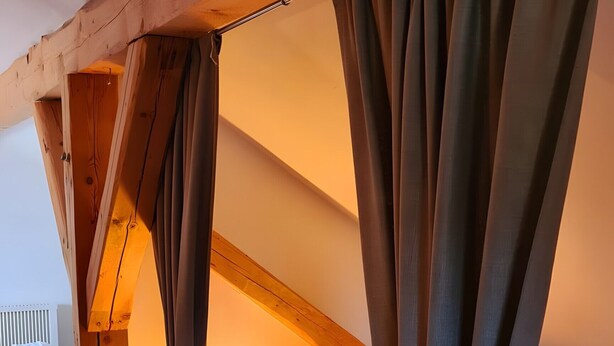 Een gezellige slaapkamer met een bed, nachtkastje, lamp en gordijnen.