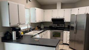 Una cocina moderna con armarios blancos, encimera negra, electrodomésticos de acero inoxidable y suelo de baldosas.