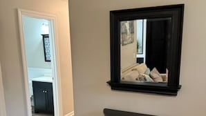 Un pasillo con suelo de madera, una consola negra y un espejo en la pared.