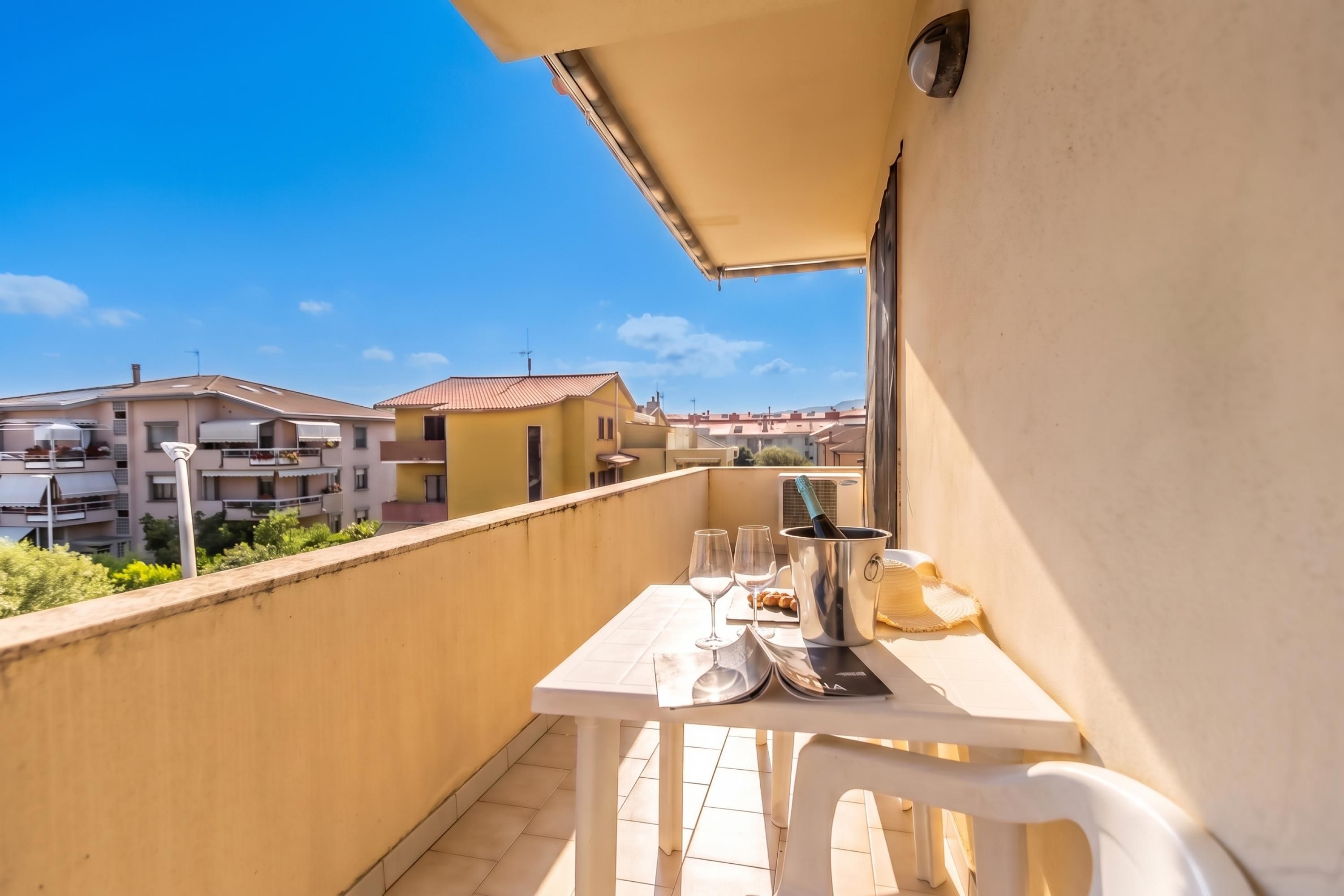 A balcony with a table, two glasses, a bottle of champagne, and a straw hat.