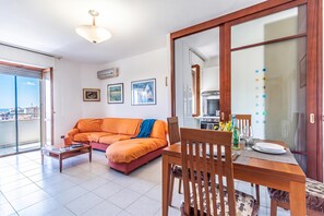 Una sala de estar moderna con un sofá, una mesa de comedor y una cocina visible a través de una puerta de vidrio.