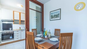 A dining area with a wooden table set for four, surrounded by wooden chairs. A kitchen with modern appliances is visible in the background. - Casa Gialla (Alghero)