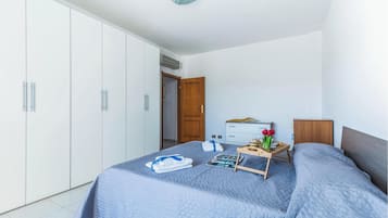 Un dormitorio con cama, una mesita de noche con una bandeja de objetos, un armario y una puerta que da a otra habitación.