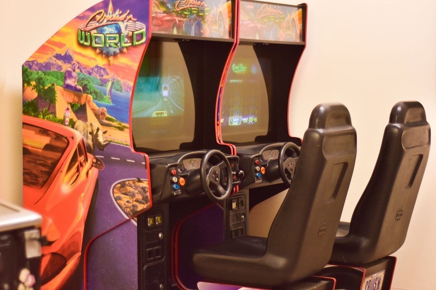 A racing arcade game setup with two steering wheels, a dashboard, and a screen displaying a race.