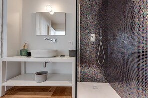 A modern bathroom with a white vanity, a large mirror, a sink, and a shower with a mosaic tile wall.
