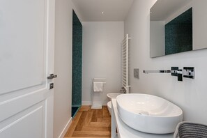 A modern bathroom with a large white sink, a toilet, and a shower.