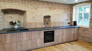 A kitchen with a brick wall, wooden cabinets, a built-in oven, and a window with a view. - Holiday Home 'Alte Schlosserei' with Private Terrace, Private Garden and Wi-Fi (Presseck)