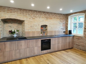 Una cocina con pared de ladrillo, armarios de madera, horno empotrado y ventana con vistas.