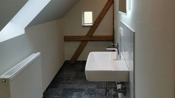 A narrow, sloped hallway with a skylight, a white radiator, a sink with a mirror, and patterned floor tiles.