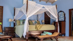 A four-poster canopy bed with a wooden frame and white netting, a wooden bench with a woven seat, and a patterned floor. - 5 Bedroom Waterfront Villa Tryst (Northside)
