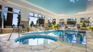 Un área de piscina interior moderna con vistas despejadas al exterior, incluyendo árboles y una montaña al fondo.