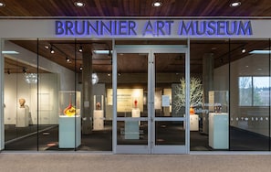 The Brunnier Art Museum entrance with glass doors, a wooden ceiling, and a sign above the doors.