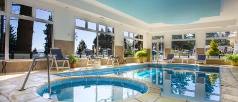 Un área de piscina interior moderna con vistas despejadas al exterior, incluyendo árboles y una montaña al fondo.