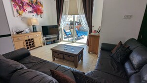 A living room with a sofa set, a coffee table, a TV, and a painting on the wall. - Ennazuse - Beautiful 2 Bedroom Villa in Pernera (Paralimni)