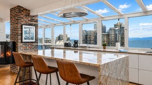 A modern kitchen with a large island, bar stools, a fireplace, and a city view.