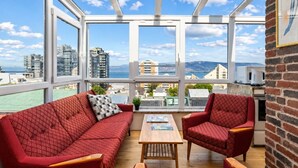 A high-rise apartment with a large balcony, red patterned furniture, and a view of the cityscape.