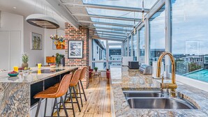 A modern kitchen with a large island, bar stools, a stainless steel sink, and a view of the city through large windows.