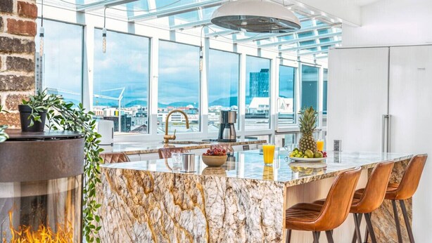 A modern kitchen with a marble island, large windows, and a city view.