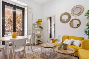A bright living room with a yellow sofa, white chairs, a wooden coffee table, and a bookshelf. - Yellow Lavapies (Madrid)
