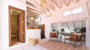 A spacious living area with a high ceiling, wooden beams, a dining table with chairs, and a cozy seating area with cushions.