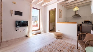 A spacious living room with a TV, a large window, and a kitchen area with a microwave and sink.