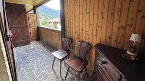 A wooden cabin with a stone floor, wooden walls, a balcony with a view of mountains, and a small table with a lamp. - 012 Trilocale Pinzolo (Pinzolo)